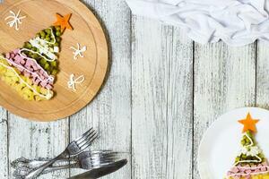 Christmas tree from a salad olivier in plate on a white wooden table. Top view with a copy space photo