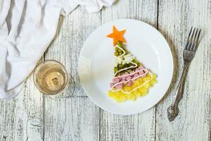 Christmas tree from a salad olivier in plate on a white wooden table. Top view with a copy space photo