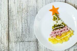 Christmas tree from a salad olivier in plate on a white wooden table. Top view with a copy space photo