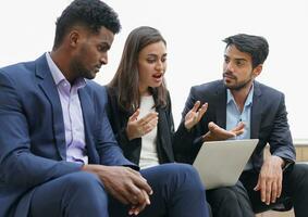 multiethnic business people in suits working outdoors site, sitting and working over the internet, businesswoman having conflict while discussing on laptop photo