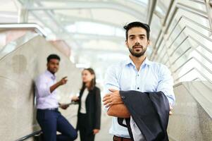 young executive standing with arms crossed, background are employee talking about him as bullying. concept for management conflict in the workplace photo