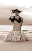 This is not - In a classic hula pose, a man hula dancer kneels on the wet beach beside the ocean. photo