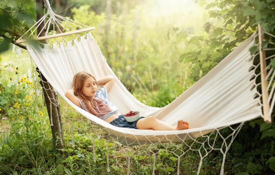 A little girl rests in a hammock and eats cherries in the summer. photo