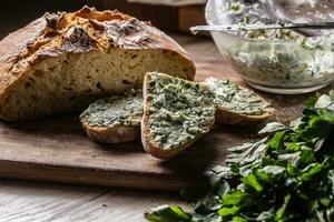 Herb butter spread on slices of fresh, home made crusty bread with green herbs aside photo