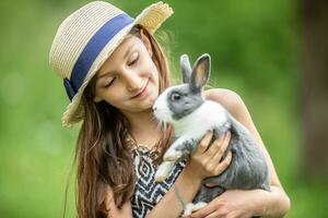 Young kid happily holding a grey rabbit in hands and playing with it photo
