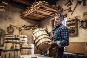 Craftsman puts finished wooden barrel on a table in his rustic workshop photo