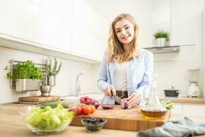 Young happy blonde girl preparing healthy salad in home kitchen photo