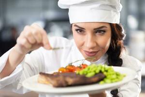 Professional female chef in a hat makes final touches on a freshly made steak before serving photo