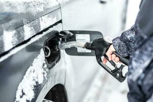 mano de un hombre relleno arriba el combustible tanque de su coche durante congelación Nevado invierno foto