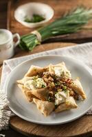 Fried pierogi served on a plate with bryndza cheese, bacon, and chives photo