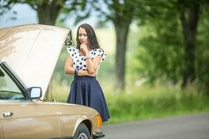 Woman in need for assistance desperately looking down to an open hood car engine after a breakdown photo