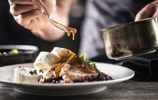 Detail of chef's hand pouring sauce over pork slice with dumplings and red cabbage photo