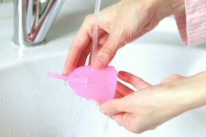 a young woman washes a menstrual cup in the bathroom photo