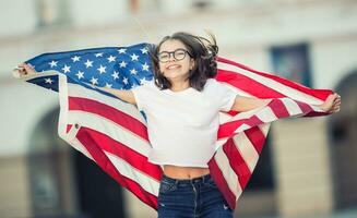 Happy young american school girl holding and waving in the city with USA flag photo