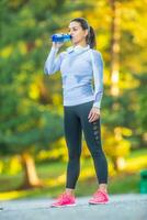 Young female athlete drinks water after training. photo