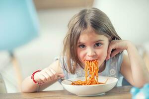 Cute little kid girl eating spaghetti bolognese at home photo