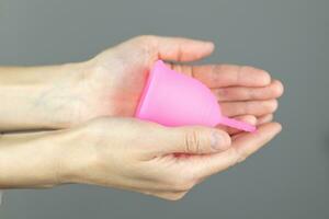 de cerca de un mujer manos participación un silicona menstrual taza. alternativa ecológico femenino higiene producto durante menstruación libre de desperdicios concepto foto