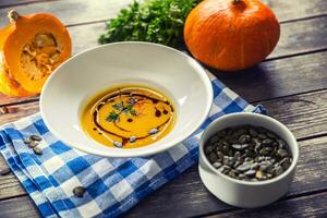 Pumpkin cream soup with seeds and parsley on kitchen table photo