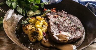 Juicy beef Rib Eye steak roasted potatoes with sauce grilled vegetable salt pepper and herbs in vintage pan photo