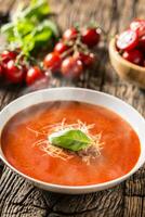 Hot tomato soup parmesan cheese and basil leave on old oal table photo