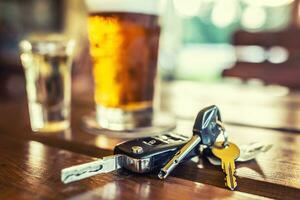 Car keys and glass of beer or distillate alcohol on table in pub or restaurant photo