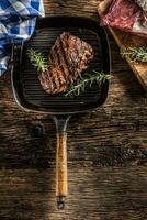 Grilled beef steak in grill pan with herbs rosemary on wooden table photo