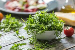 Fresh arugula salad in white dish on wooden table photo