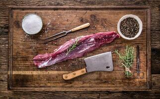 Raw beef meat. Raw beef tenderloin steak on a cutting board with rosemary pepper salt in other positions. photo