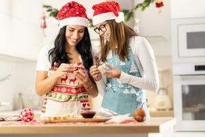 A mother and her teenage daughter dressed in Christmas aprons are making Christmas cookies at home in the kitchen photo