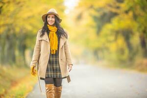 Smiling female having an autumn walk outdoors surrounded by yellow trees photo