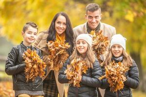 padres con un hijo y gemelo muchachas sostener vistoso hojas al aire libre en el otoño foto