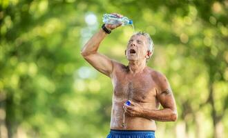 Refreshing elderly man pours water over him in the green forest to cool down on a hot sunny day photo