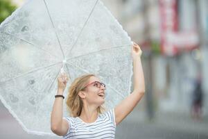 Beautiful young blonde girl holding umbrella in summer rain photo