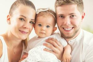 Happy young family with mother, father and baby daughter all smiling into the camera photo