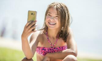 Happy young girl with dental braces making selfhie on beach in summer hot day photo