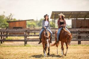 Two cowgirls riding their horses on a ranch during hot summer day photo