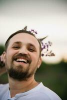 Young smiling man with bouquet of lupines like a crown. Sunset or sunrise, bright evening light photo