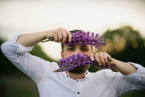 Young man with bouquet of lupines like a beard. Sunset or sunrise, bright evening light photo