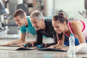 Group of people in various age and gender having fun while doing group exercise of elbow plank in the gym photo