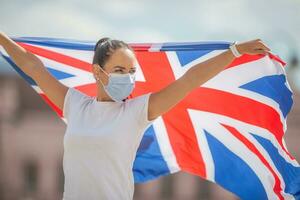 joven mujer con británico bandera usa un máscara al aire libre foto