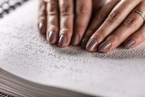 Detail of female hands of a visually impaired reader, touching the book made in braille alphabet. photo