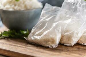 Raw rice in plastic bags on wooden background and cooked rice in bowl photo