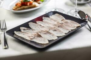 Thinly sliced veal with a tuna salsa served on a black rectangular plate photo