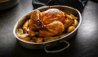 Whole baked golden crispy chicken in a pan cooked with potatoes photo