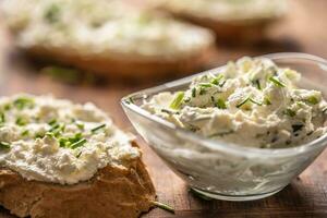 Closeup of a bowl of homemade cream cheese spread with chopped chives surrounded by bread slices with spread and a bunch of freshly cut chives photo