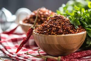 Dried and crushed chili peppers in wooden bowles with parsley herbs photo