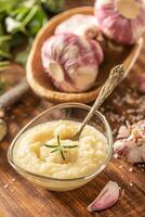 Garlic paste in a glass bowl with peeled garlic, salt, crusher and garlic heads photo