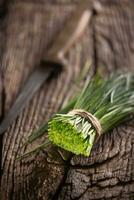 Bunch of freshly cut chives wrapped by a jute twine on a vintage wood next to a knife photo