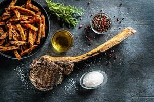 Grilled beef tomahawk steak with sweet potato fries salt spices olive oil and rosemary on rustic board - top of view photo