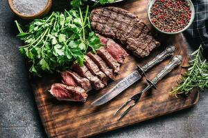 Slices of juicy grilled beef steak with fork and knife on a butcher plate photo